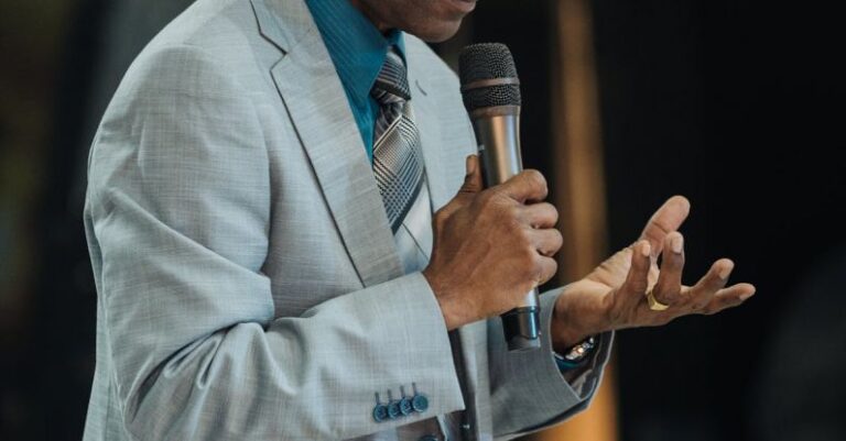 Speeches - A man in a suit and tie speaking into a microphone